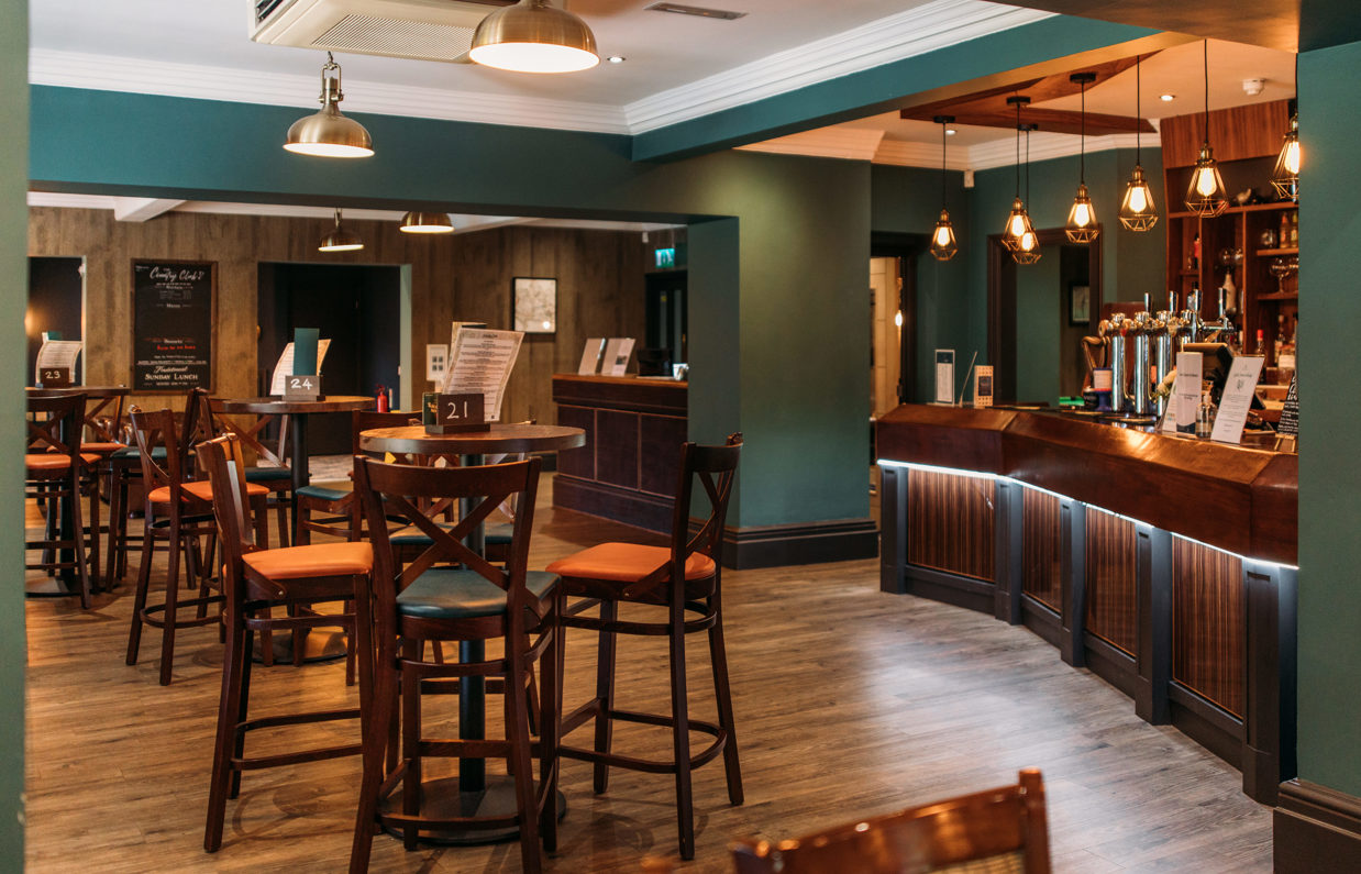 The inside of The Country Club with high tables and chairs and a bar with dramatic lighting