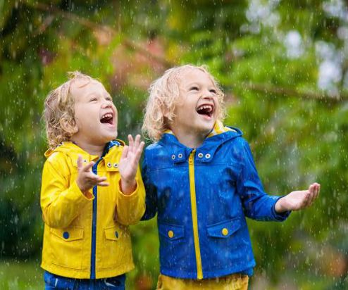 Two children out in the rain in rain coats smiling