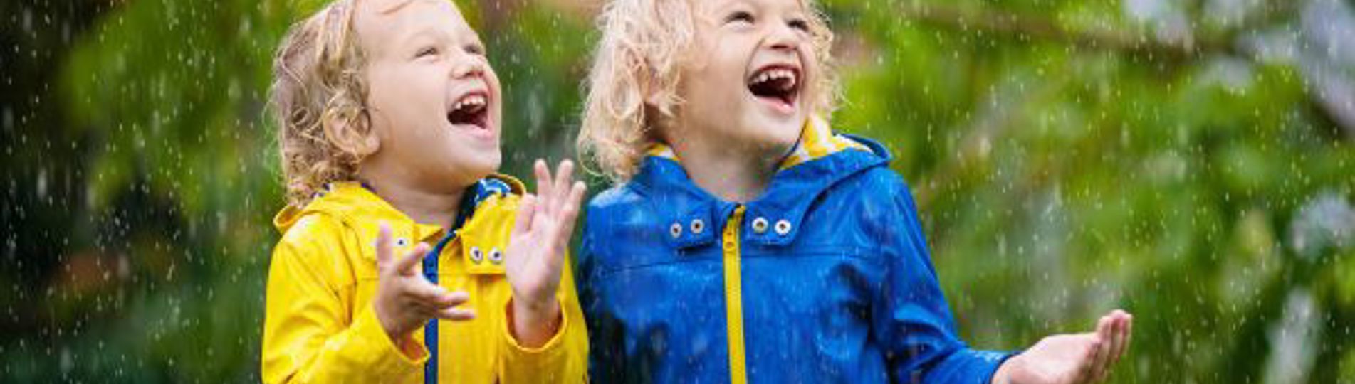 Two children out in the rain in rain coats smiling