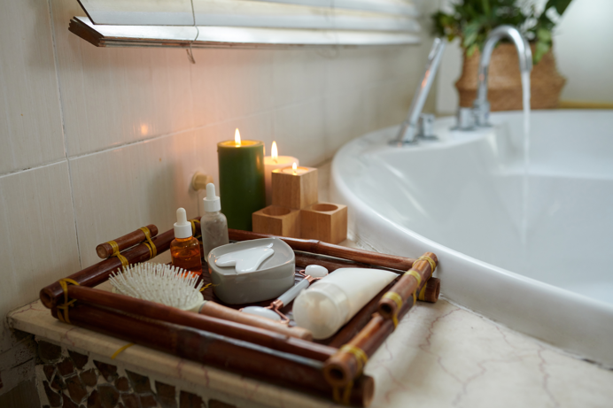 A bath with a running tap with a range of wellness and self-care items beside it