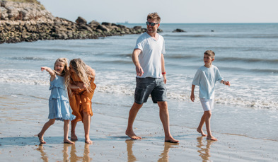Family happily walking along the beach barefoot