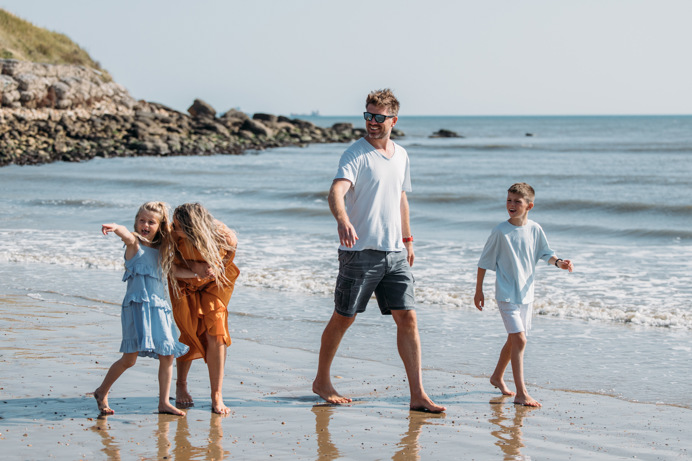 Family happily walking along the beach barefoot