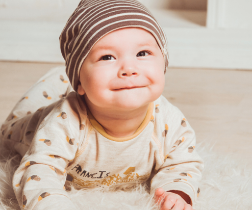 A young baby on its tummy on the floor smiling at the camera