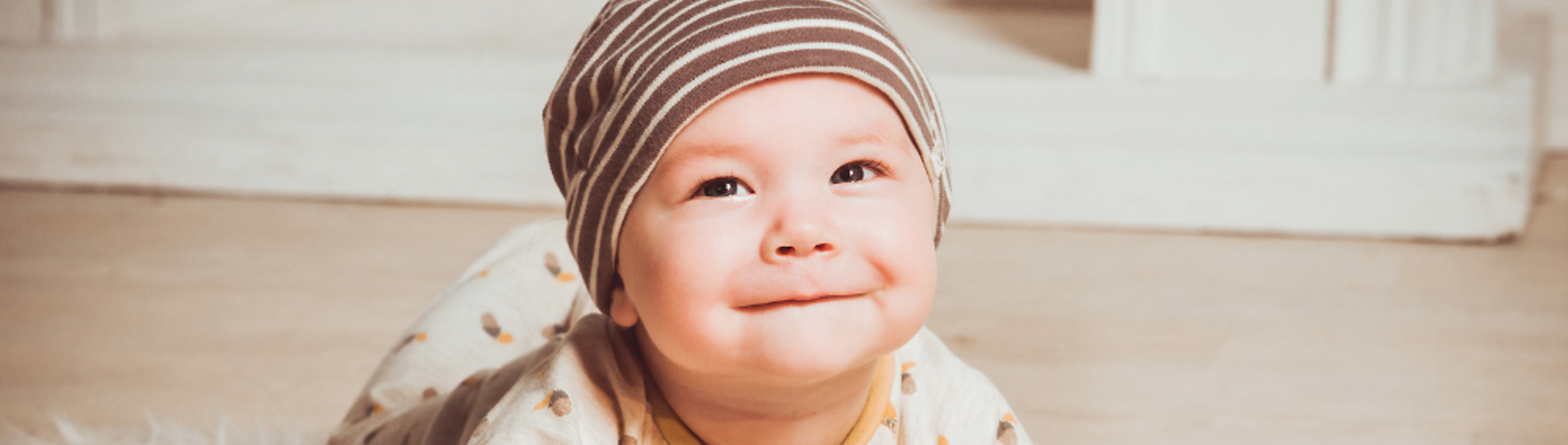 A young baby on its tummy on the floor smiling at the camera