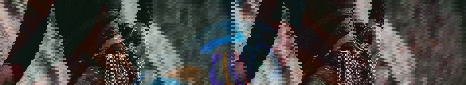 A man's body against a cliff face rock climbing with various ropes, equipment and harnesses round his waist