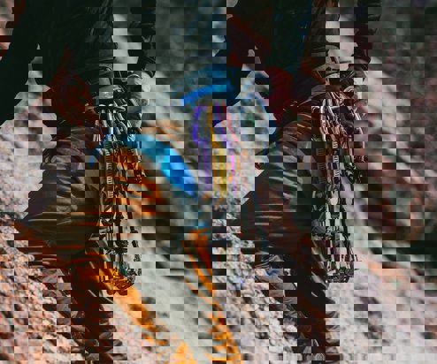 A man's body against a cliff face rock climbing with various ropes, equipment and harnesses round his waist