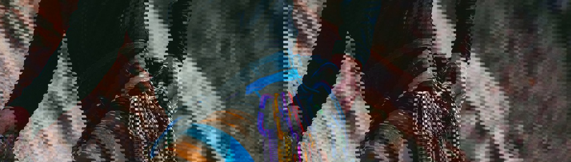 A man's body against a cliff face rock climbing with various ropes, equipment and harnesses round his waist