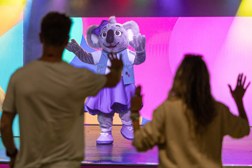 A koala mascot, Kimi on stage in an entertainment venue with a couple copying her dancing