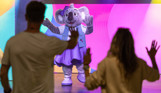 A koala mascot, Kimi on stage in an entertainment venue with a couple copying her dancing