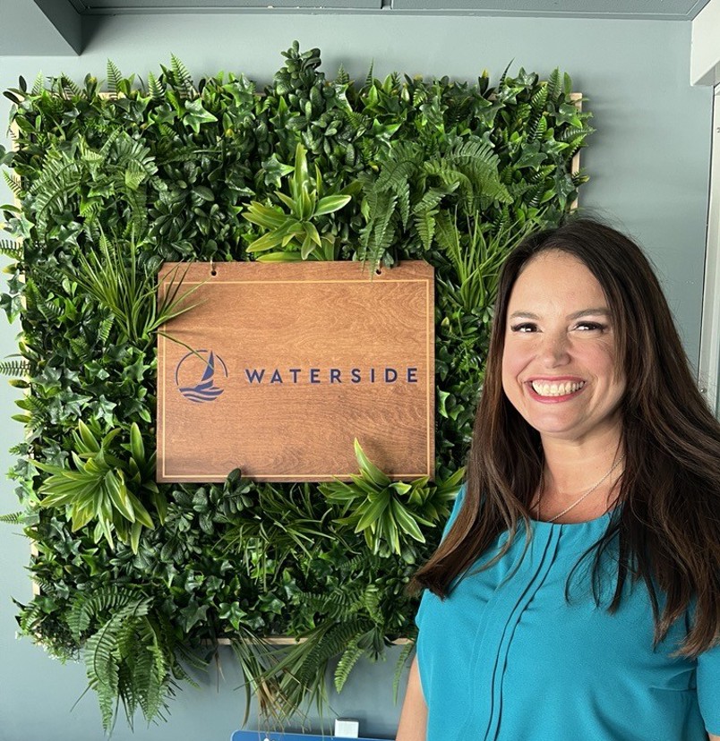 A smiling lady stood beside a Waterside sign