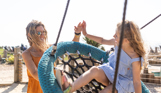 Mother and daughter high five as the mother pushes her daughter on a large rope swing