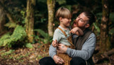 A young boy and his dad smiling together in the woods with toasted marshmallows