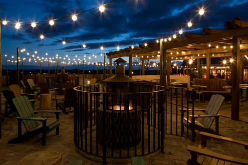 An outdoor seating area with a fire pit and chairs and fairy lights under a veranda at night