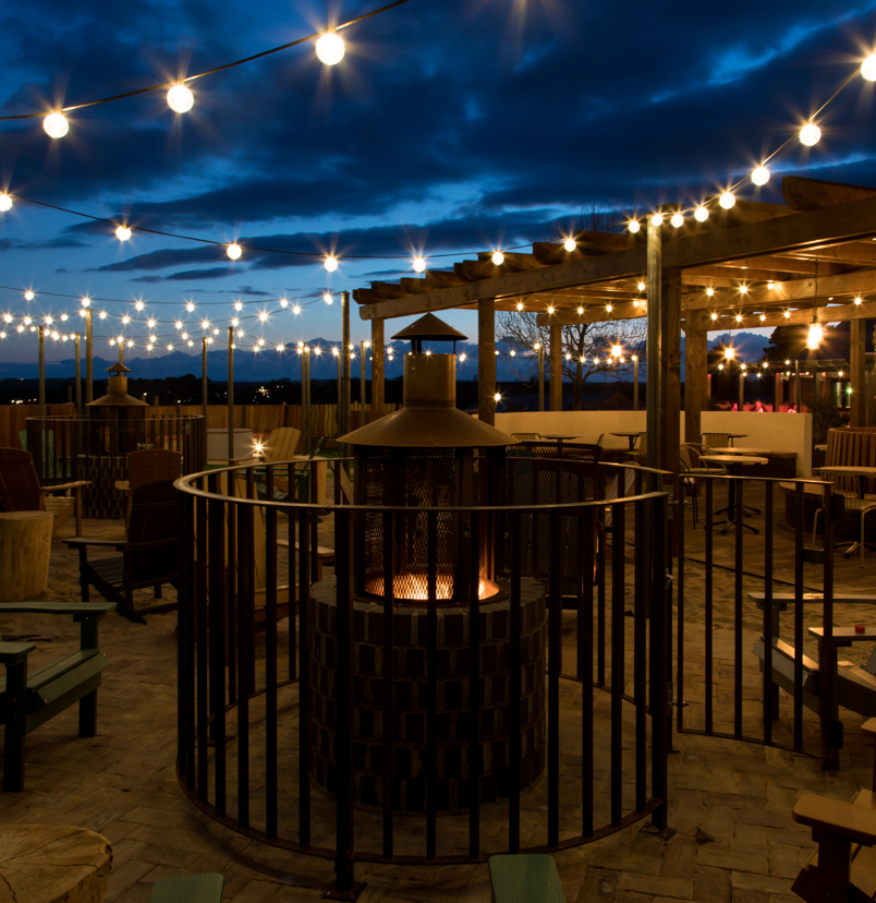 An outdoor seating area with a fire pit and chairs and fairy lights under a veranda at night