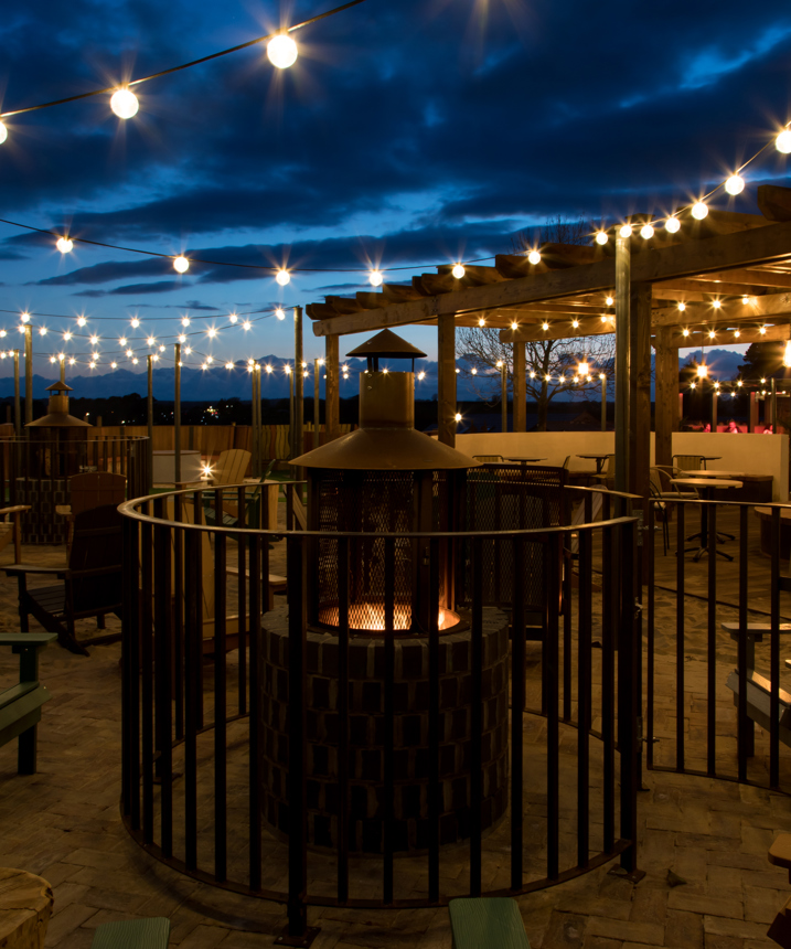 An outdoor seating area with a fire pit and chairs and fairy lights under a veranda at night