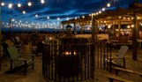 An outdoor seating area with a fire pit and chairs and fairy lights under a veranda at night