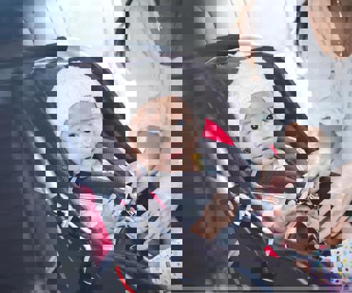 A young child in a car seat being strapped in by a lady