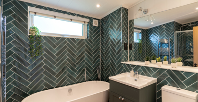 Modern bathroom with bath tub, shower, WC and sink with green herrringbone tiles