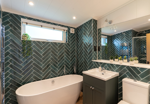 Modern bathroom with bath tub, shower, WC and sink with green herrringbone tiles