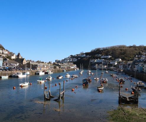 A harbour with various small boats, hills and houses on a sunny blue sky day
