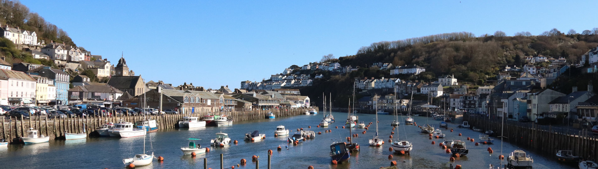 A harbour with various small boats, hills and houses on a sunny blue sky day