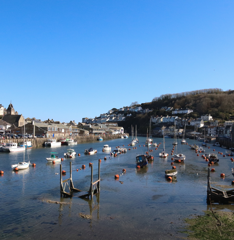A harbour with various small boats, hills and houses on a sunny blue sky day