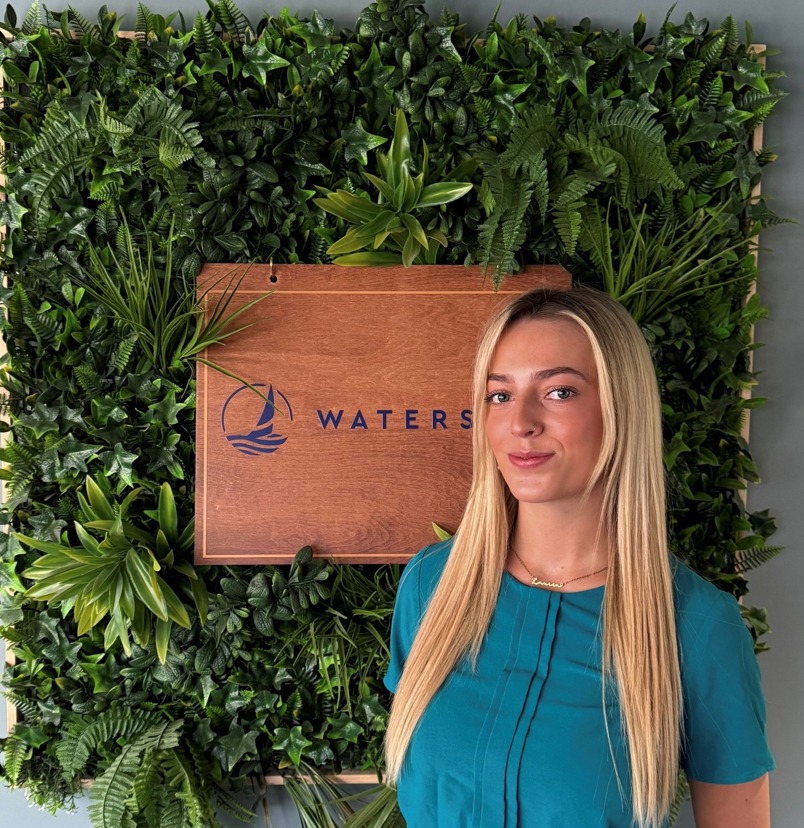 A smiling lady stood beside a Waterside sign