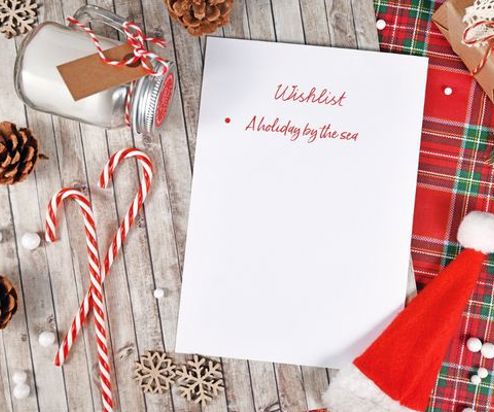 A Christmas table set from above with a wishlist on it with only one item: A holiday by the sea