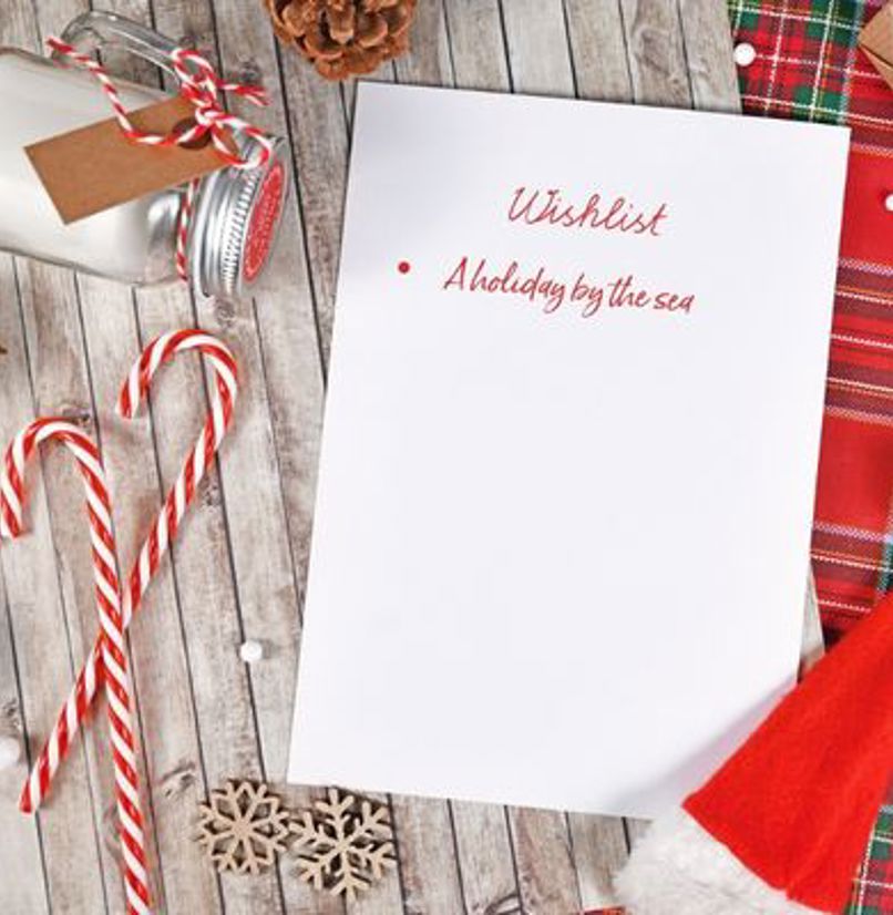 A Christmas table set from above with a wishlist on it with only one item: A holiday by the sea