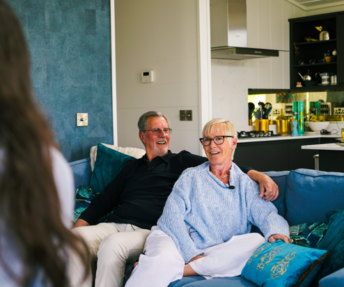 A couple sat on a sofa together looking at another woman