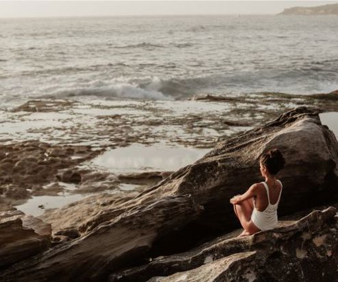 A woman sat in a swimsuit on the rocks by the sea