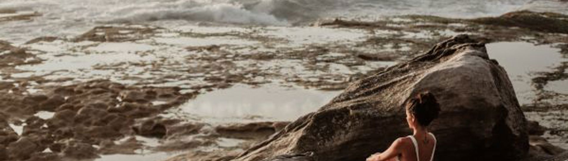 A woman sat in a swimsuit on the rocks by the sea