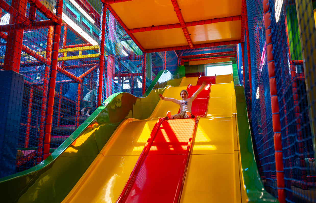 A young girl going down a large bright slide in a softplay