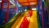 A young girl going down a large bright slide in a softplay