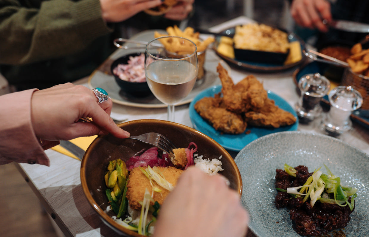 A selection of chicken, pasta, veggie and potato dishes at a table with three people eating