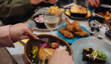 A selection of chicken, pasta, veggie and potato dishes at a table with three people eating