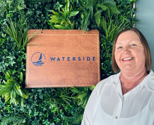 A smiling lady stood beside a Waterside sign