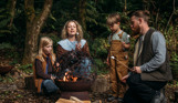 Family toasting marshmallows on fire pit in woodland