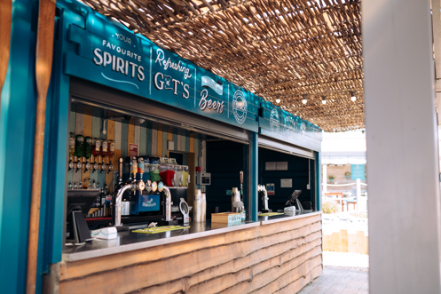 An outdoor beach drinks bar under cover with various draught, spirit and soft drinks on display