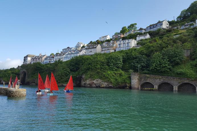 A body of water by land with various boats going out towards the sea
