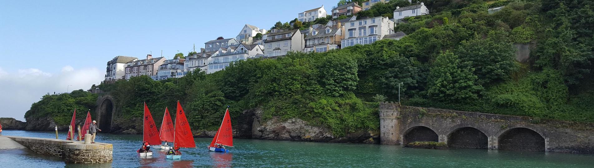A body of water by land with various boats going out towards the sea