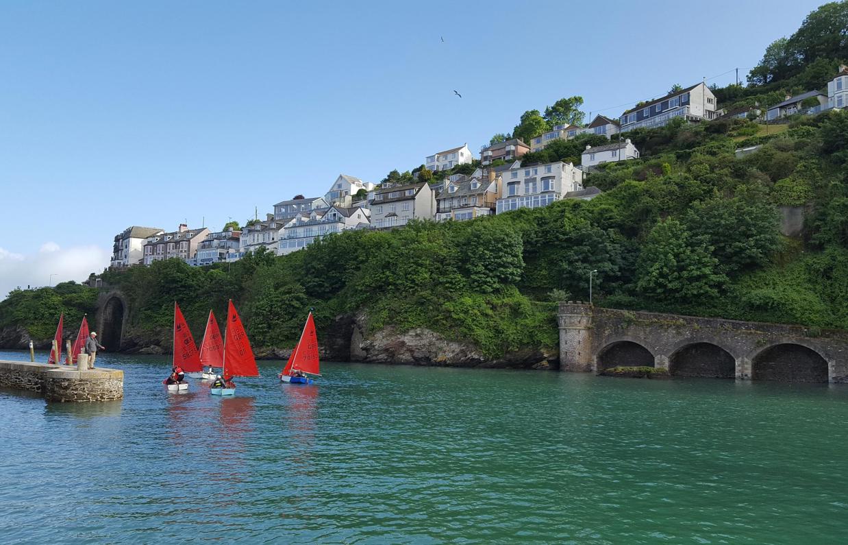 A body of water by land with various boats going out towards the sea