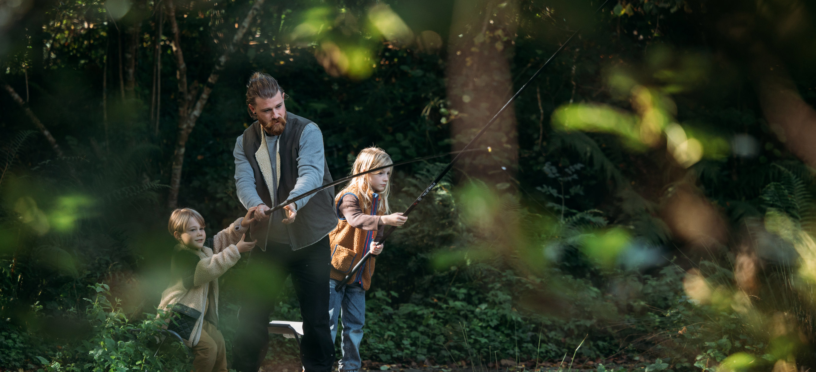 A man and his two young sons fishing by a lake in the woodland 