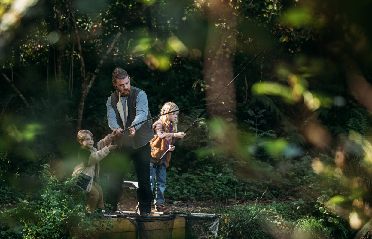 A man and his two young sons fishing by a lake in the woodland 