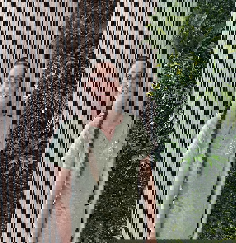 A lady smiling in spa uniform against a greenery / walnut decór background