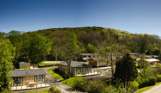 Holiday lodges among woodland at the bottom of rolling countryside hills on a sunny, blue sky day