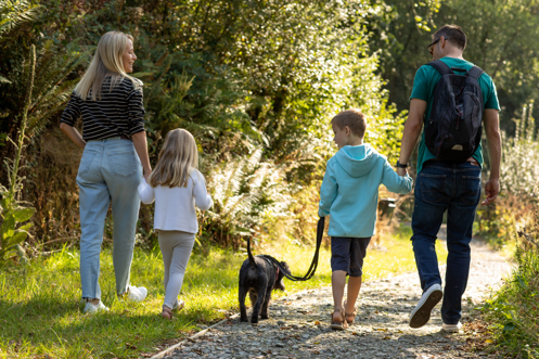 A family of four walking a small black dog on a lead around the lakes and nature trail at Tregoad Holiday Park