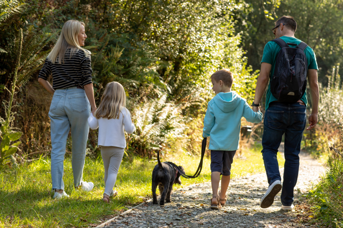 A family of four walking a small black dog on a lead around the lakes and nature trail at Tregoad Holiday Park