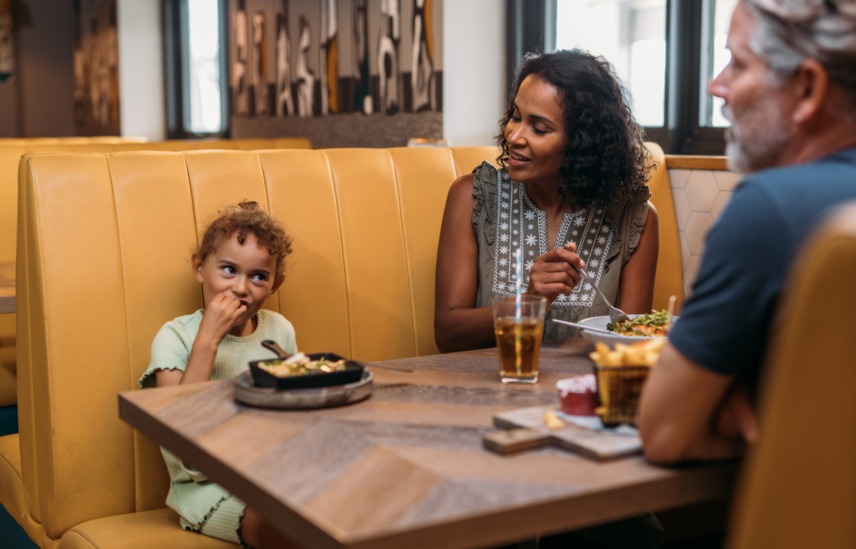A couple and a young girl sat at a booth in Breeze Bar & Grill eating and drinking
