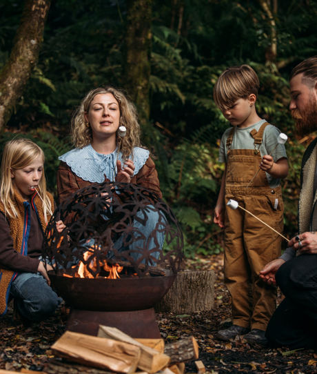 A family of four in the woods by a fire toasting marshmallows